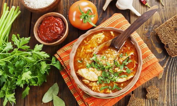 Chicken Kharcho soup in a terracotta bowl with parsley, surrounded by ingredients on a rustic table